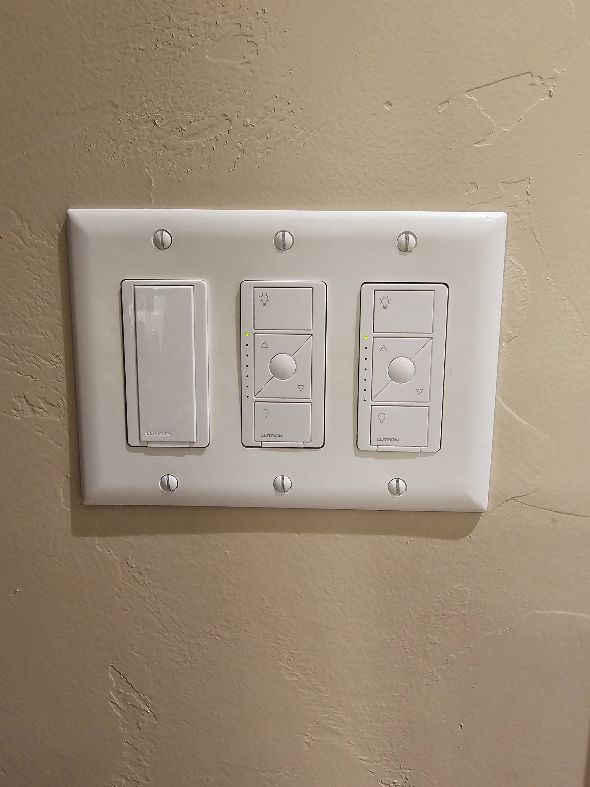 White triple light switch panel on a beige wall, with one dimmer switch and two push-button switches.