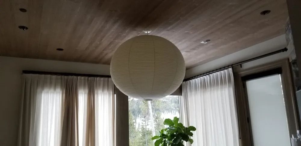 Living room with large windows, curtains, a hanging paper lantern, and a potted plant