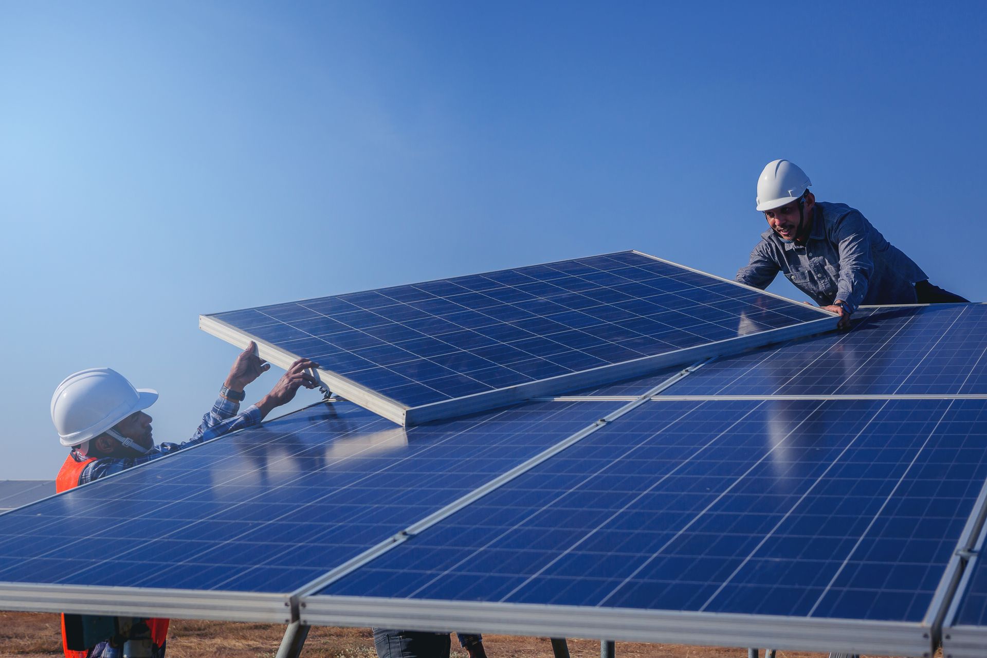 Workers installing blue solar panels on a rooftop under a clear sky