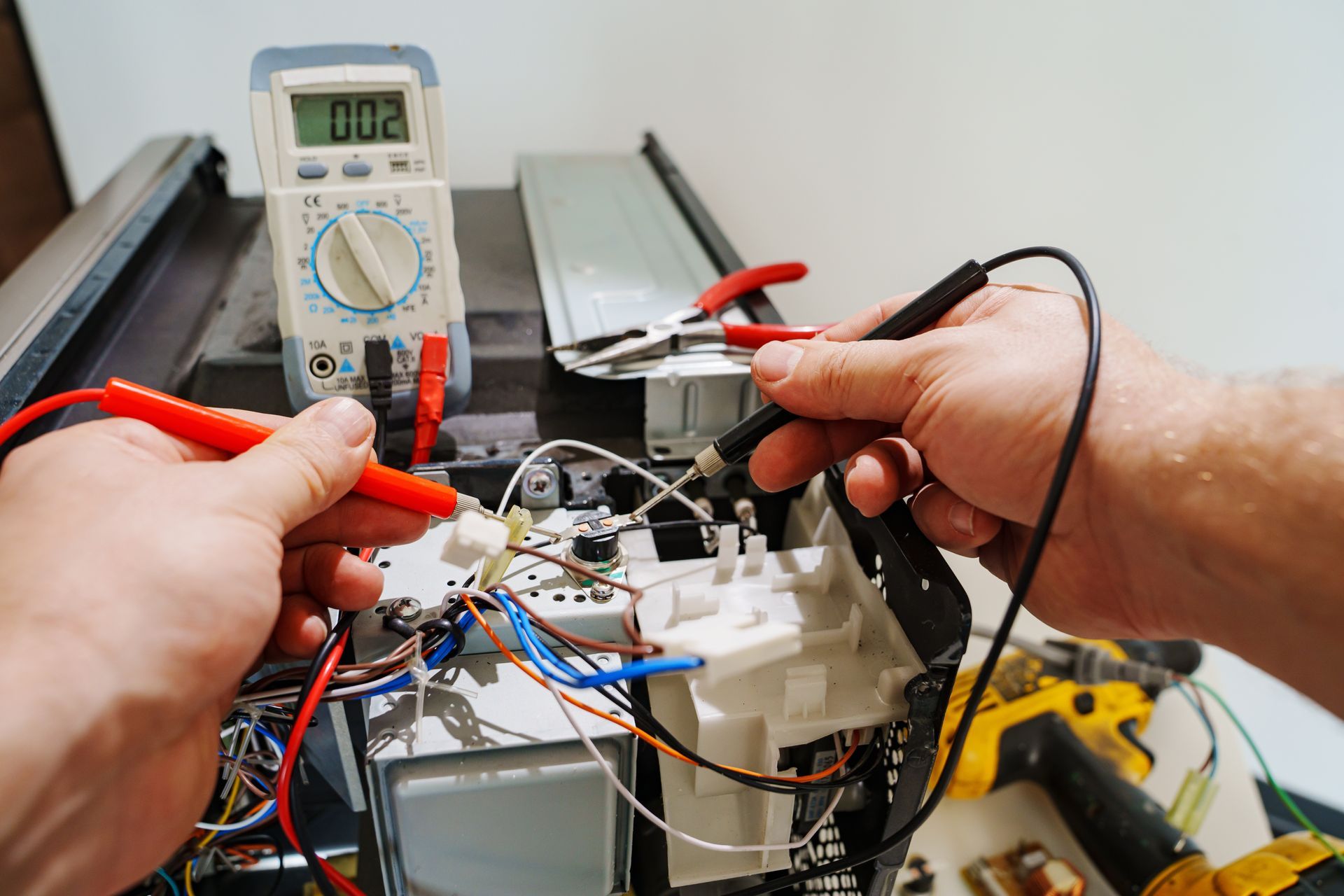 Hands testing an electronic circuit with a multimeter and probes on a workbench