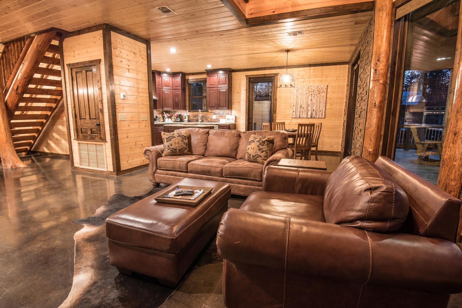 A living room with a couch , chair , ottoman and stairs.