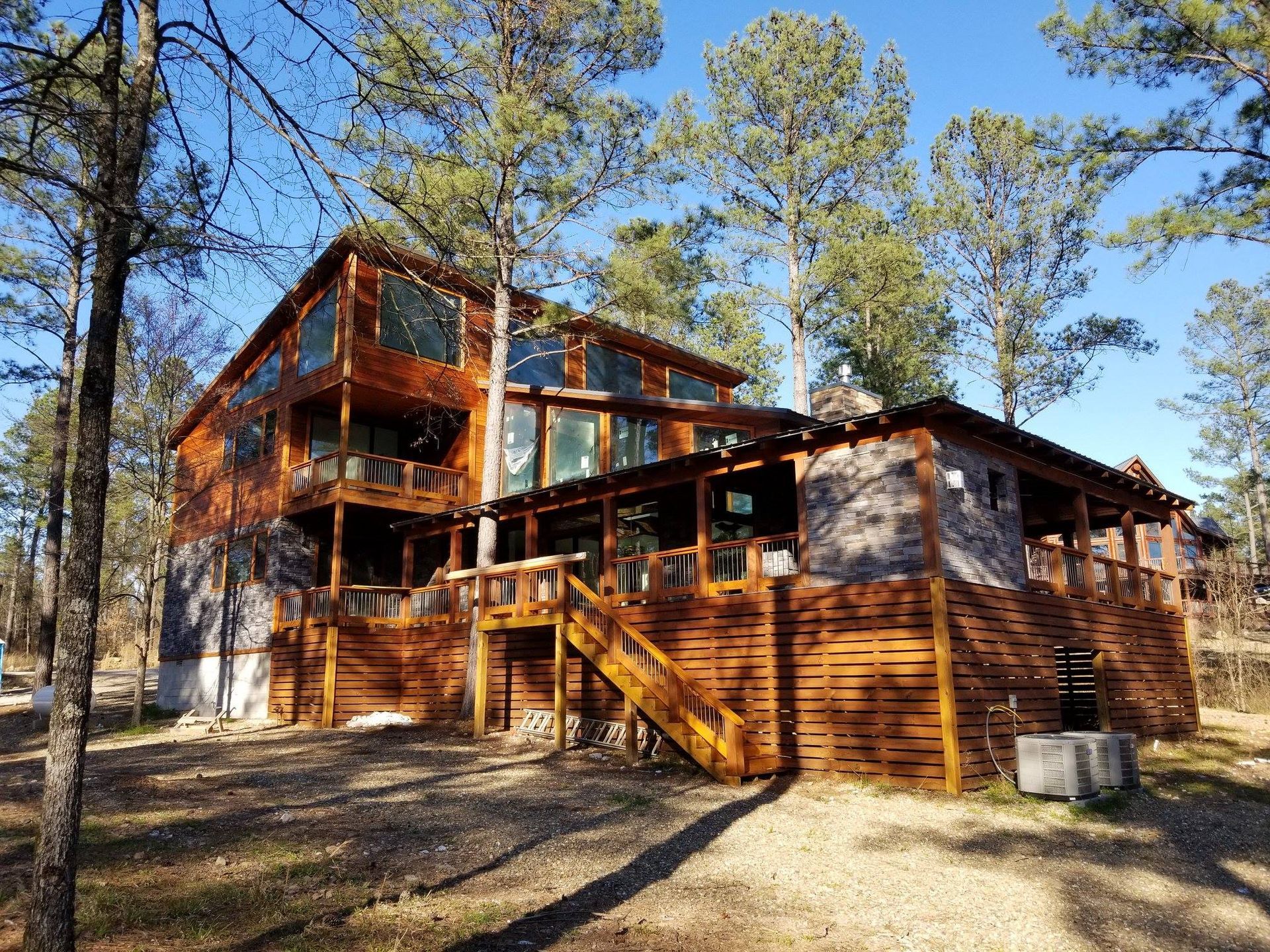 A large wooden house with a large deck in the middle of a forest.