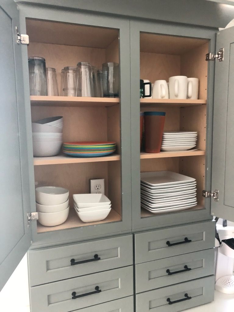 A kitchen cabinet filled with plates , bowls , cups and glasses.