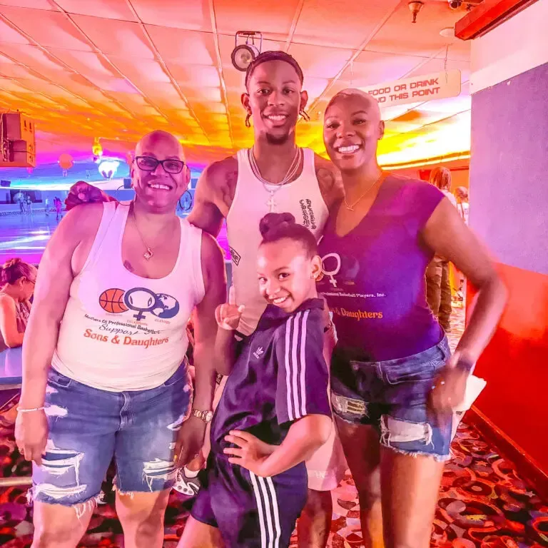 Four people smile at a roller rink. Two women, a man, and a girl pose together. Bright lighting.