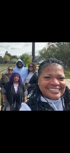 Five people smiling outdoors. One woman is in the foreground. Other people are behind her.