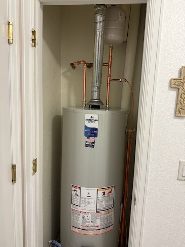 Water heater in a narrow closet with exposed copper pipes and venting.