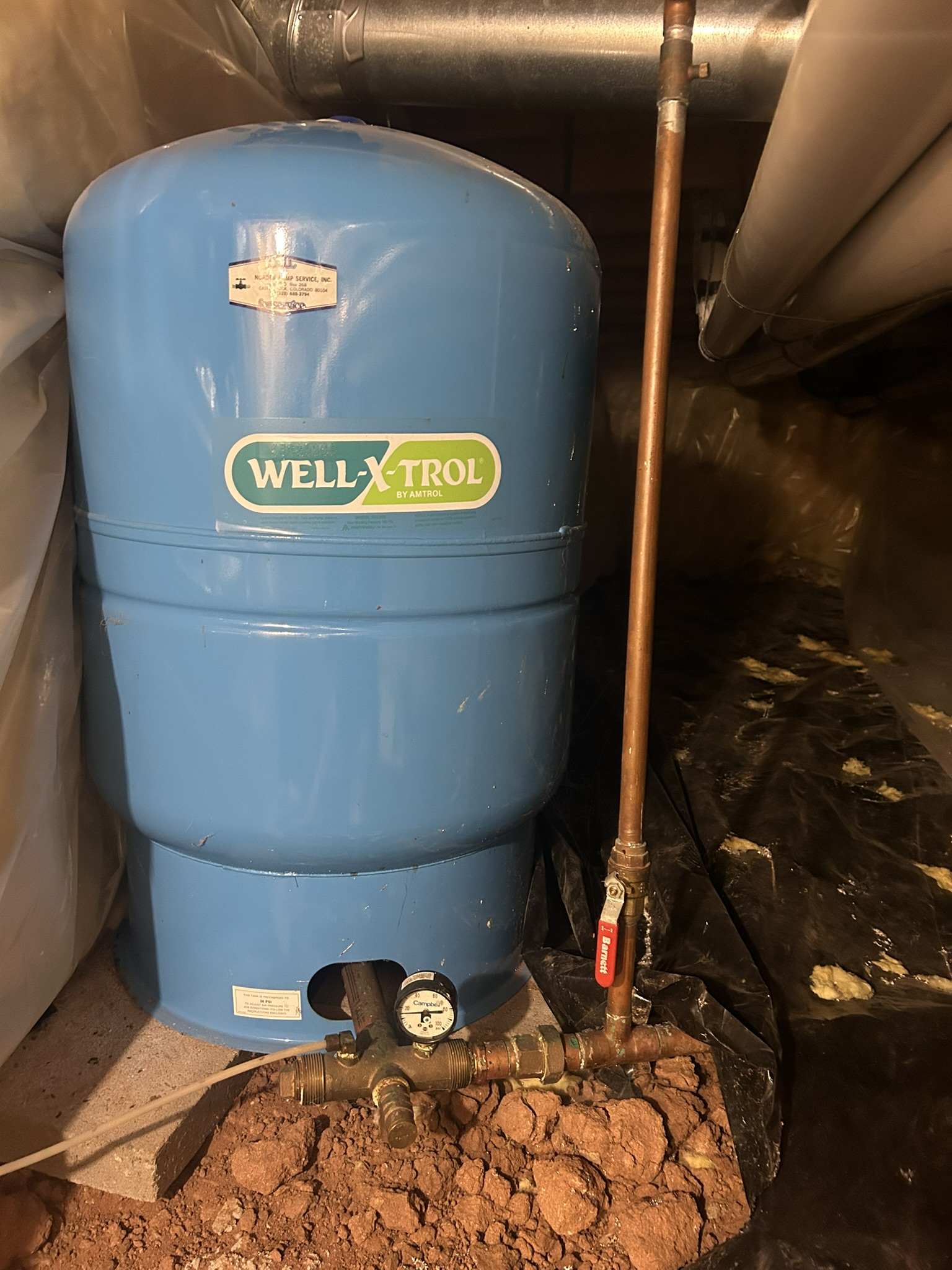 Blue WELL-X-TROL water tank and pipes in a basement utility area, with dirt on the floor.