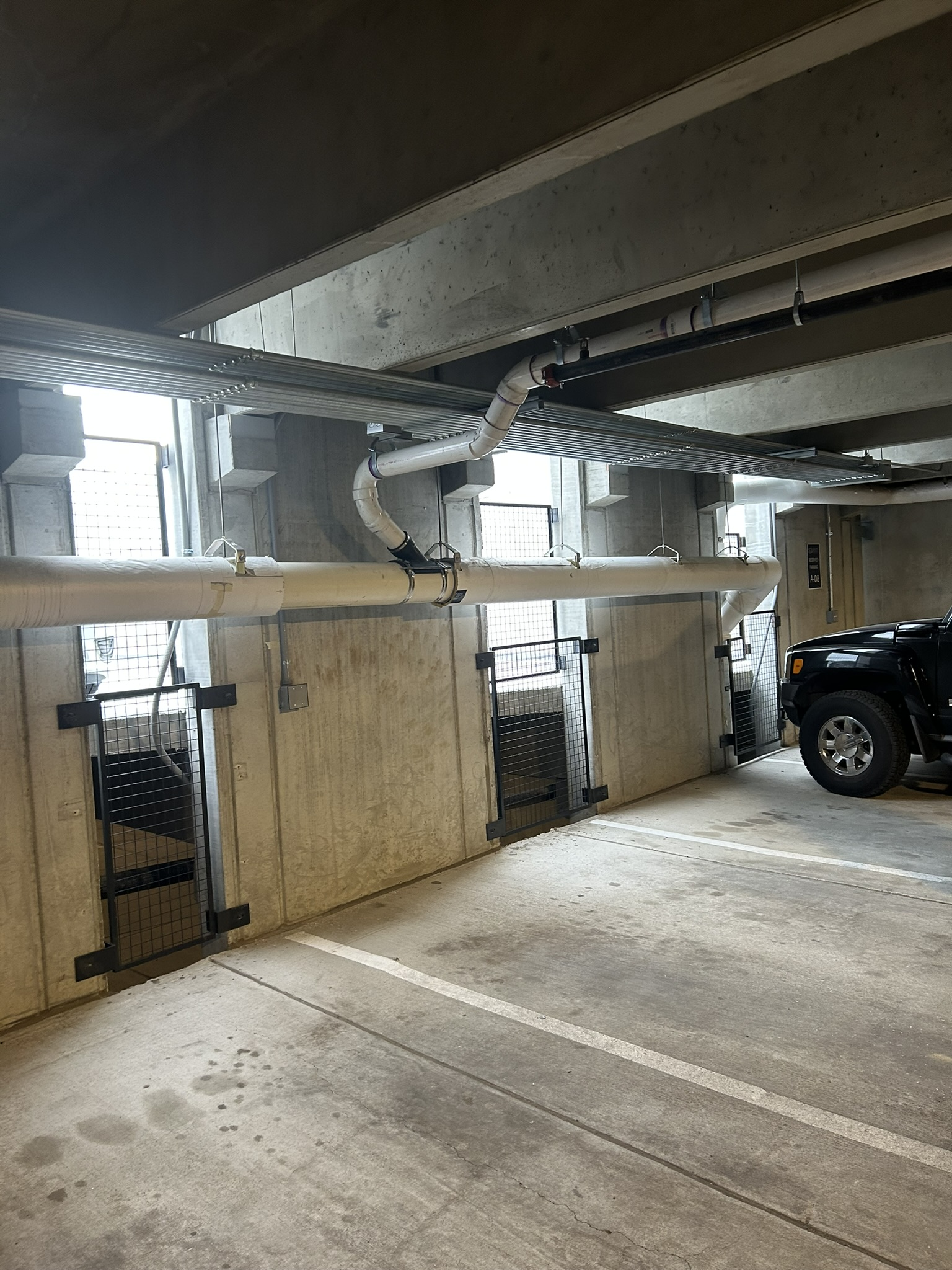 Covered parking garage with metal beams, chain-link gates, and a black SUV parked on the right.