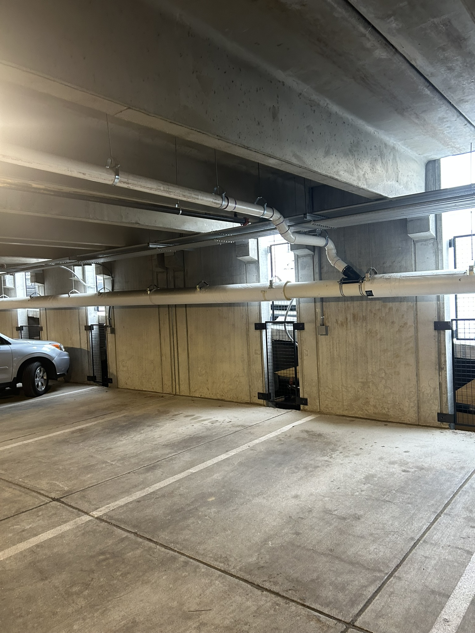 Covered parking garage with concrete pillars, a parked car, and a person standing by a wall