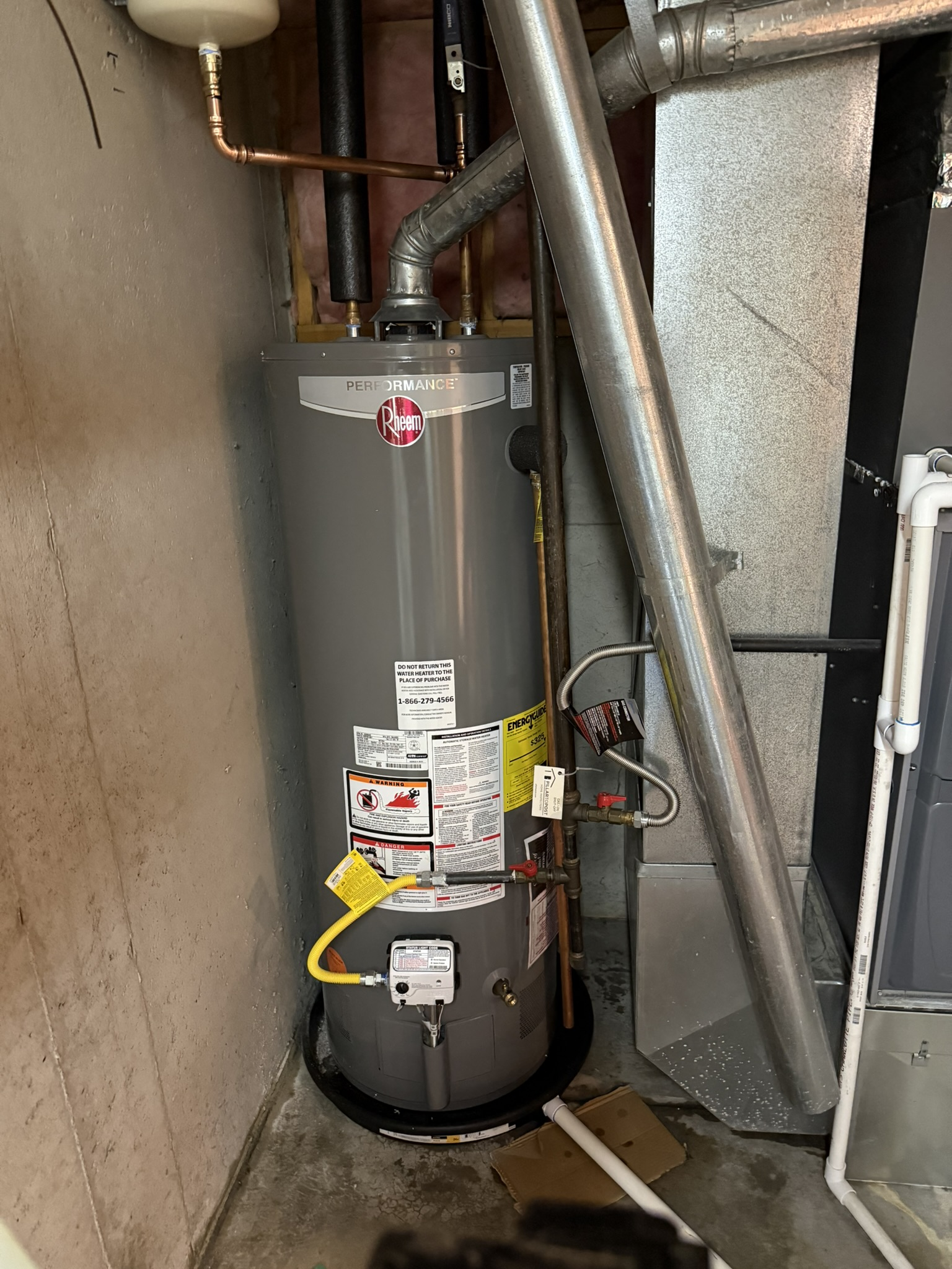 Water heater in a cramped utility closet with exposed pipes and insulation wrapping.