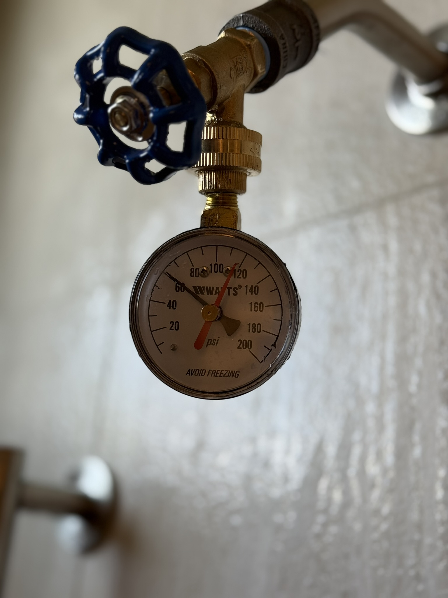 Blue-handled valve with a pressure gauge mounted on a wall pipe