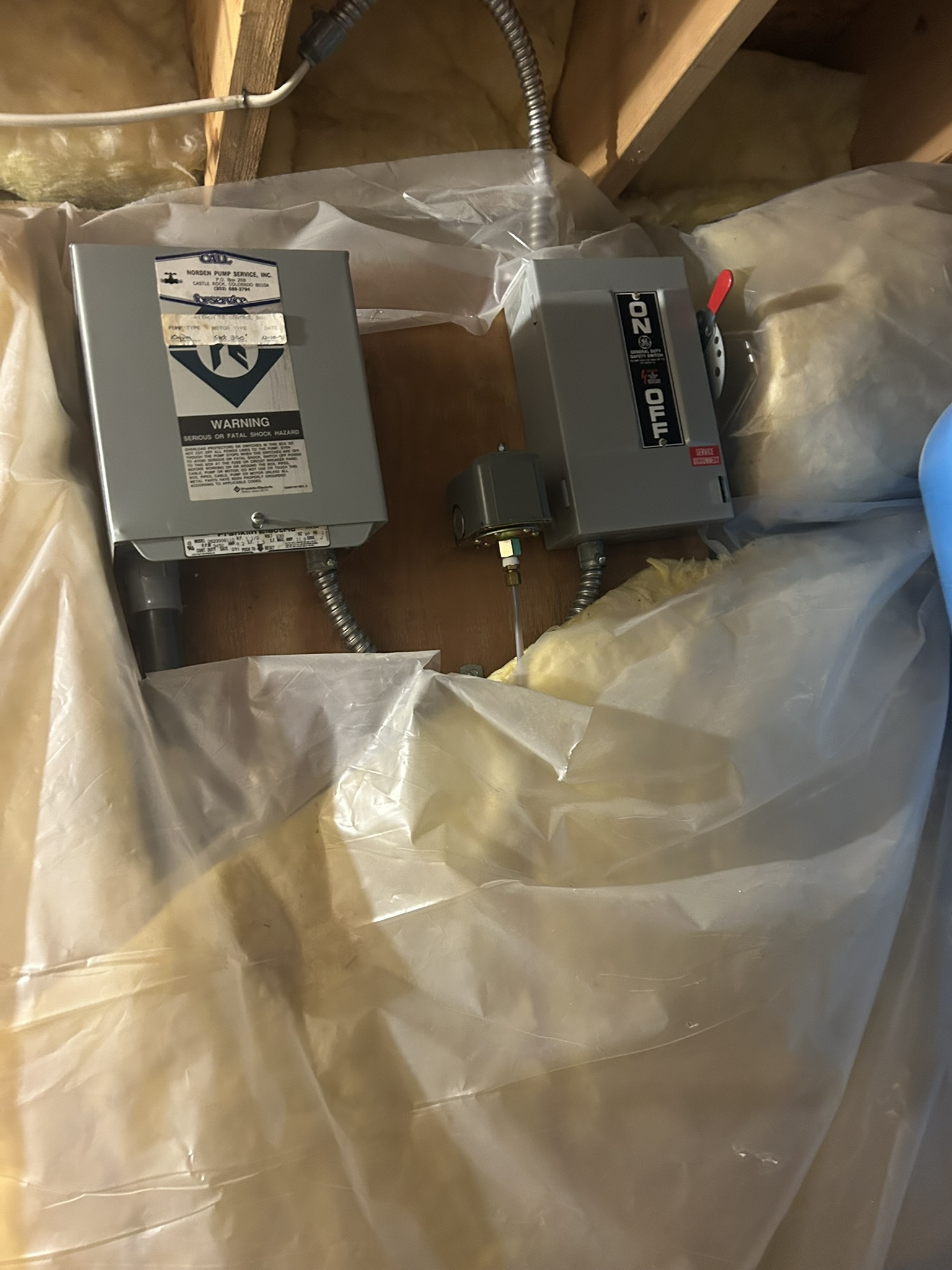 Two gray electrical devices in plastic packaging inside a cardboard box.