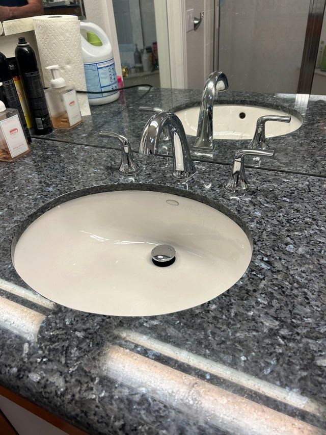 Bathroom sink with granite countertop and chrome faucet beside a toilet tank