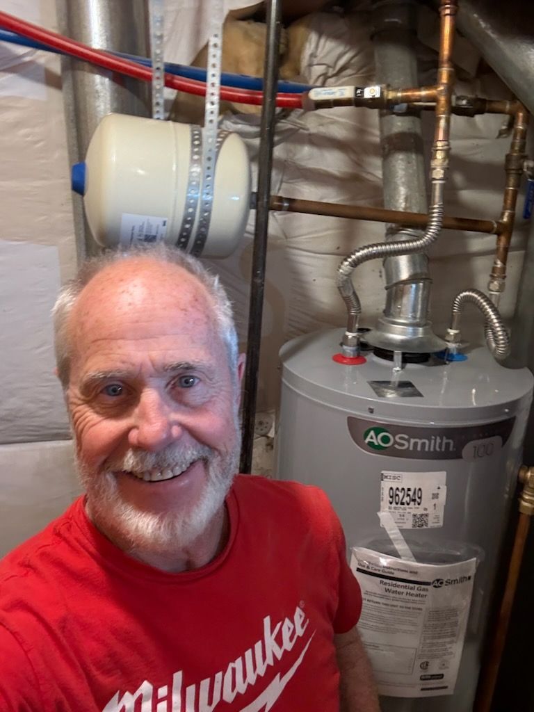 Smiling man in red shirt beside water heater and exposed pipes in a basement