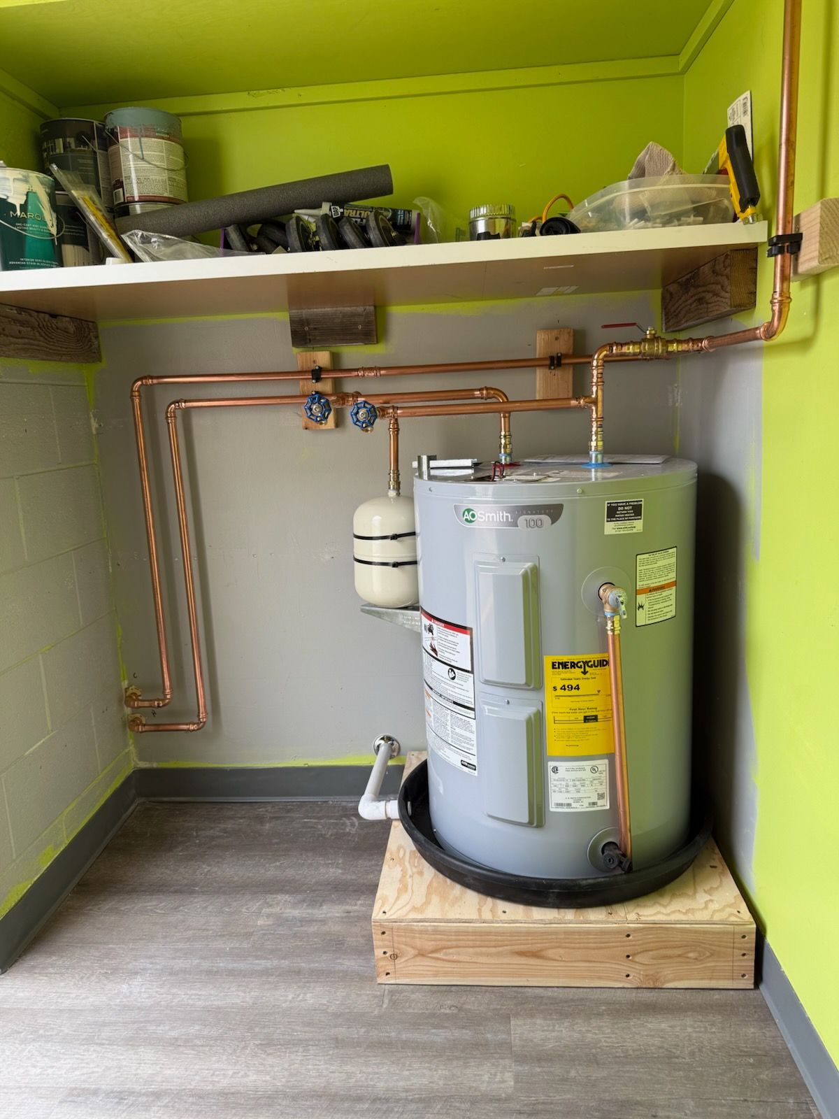 Utility closet with a water heater, copper pipes, and shelves against lime green walls