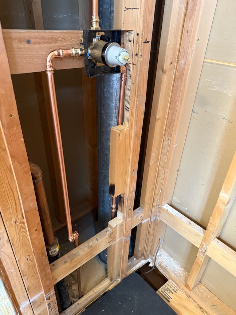 Open wall cavity with copper pipes, black vent pipe, and a valve assembly in a renovation area