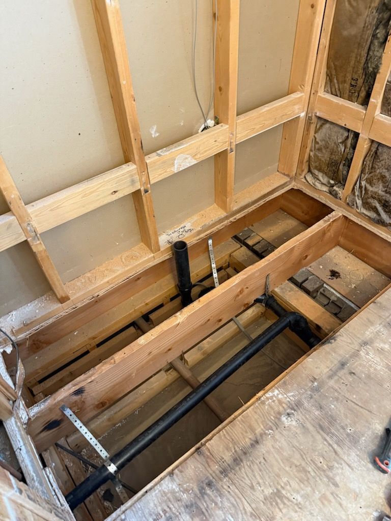 Open floor framing with exposed joists and plumbing in an unfinished room