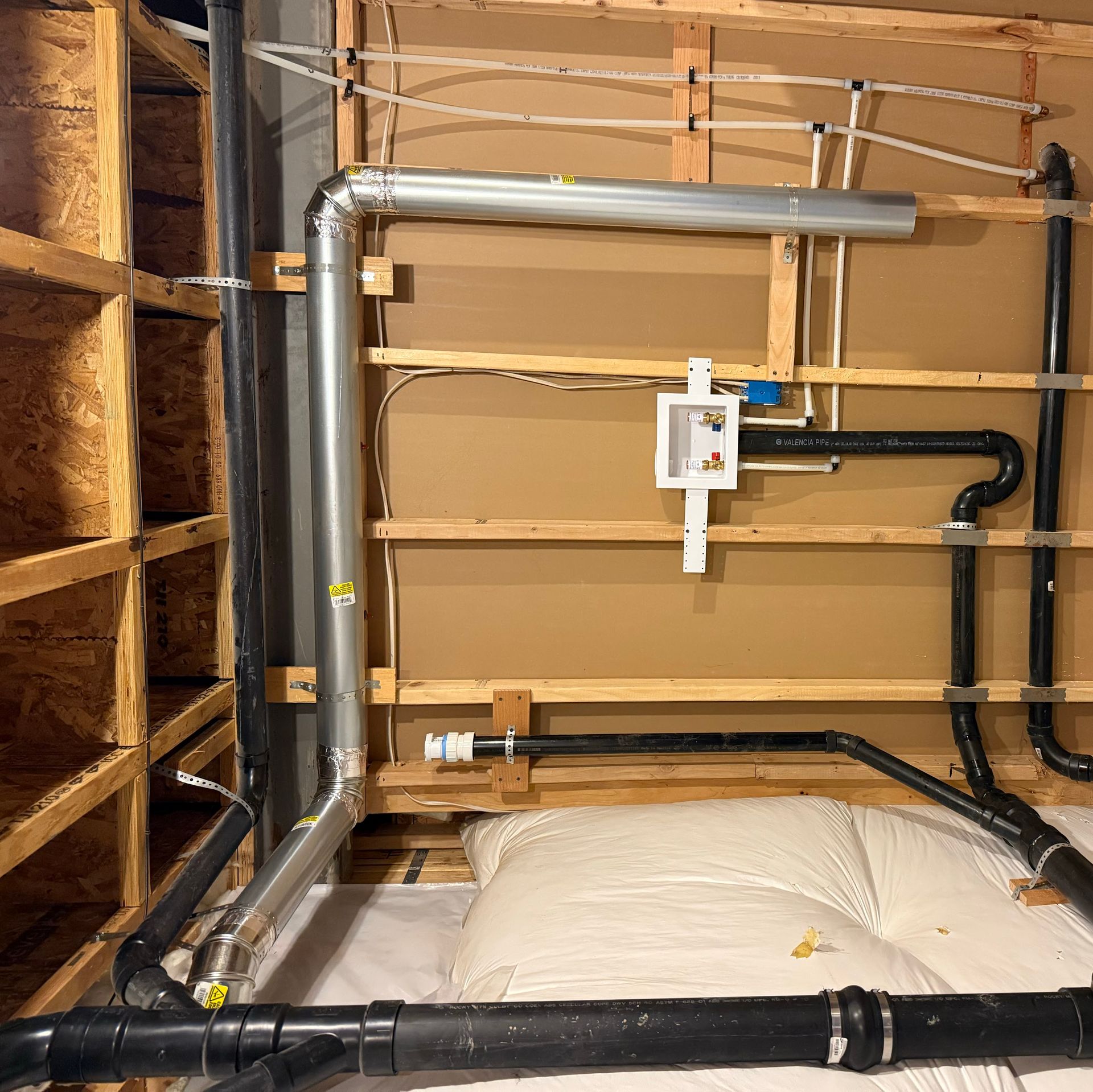Basement wall with exposed pipes, valves, and insulation behind a framed partition