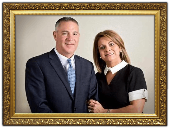 Portrait of two professionally dressed adults in a gold frame, standing together and smiling