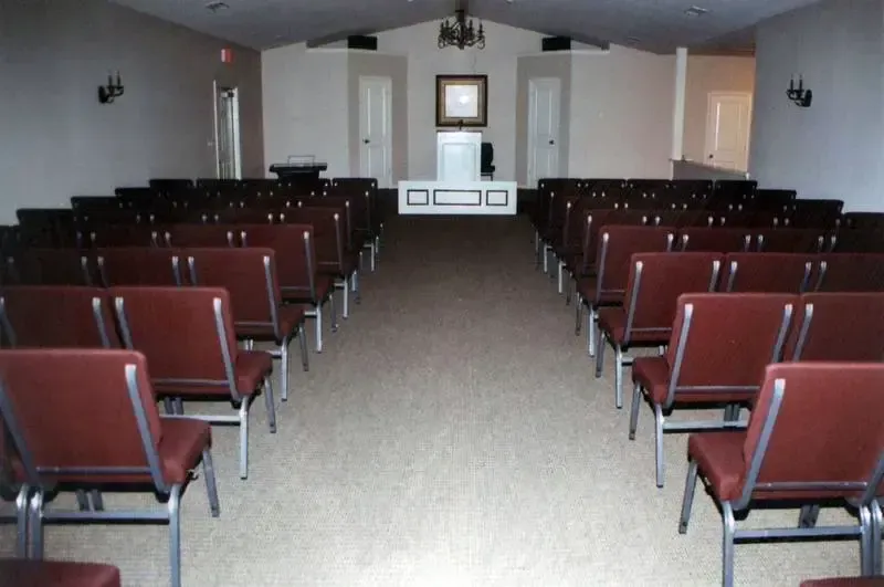 Empty auditorium with rows of red chairs facing a stage and podium at the front.