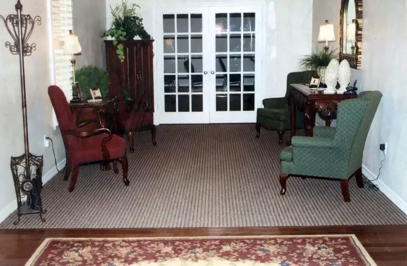 Cozy living room with two armchairs, side table, plants, and French doors to a carpeted patio area