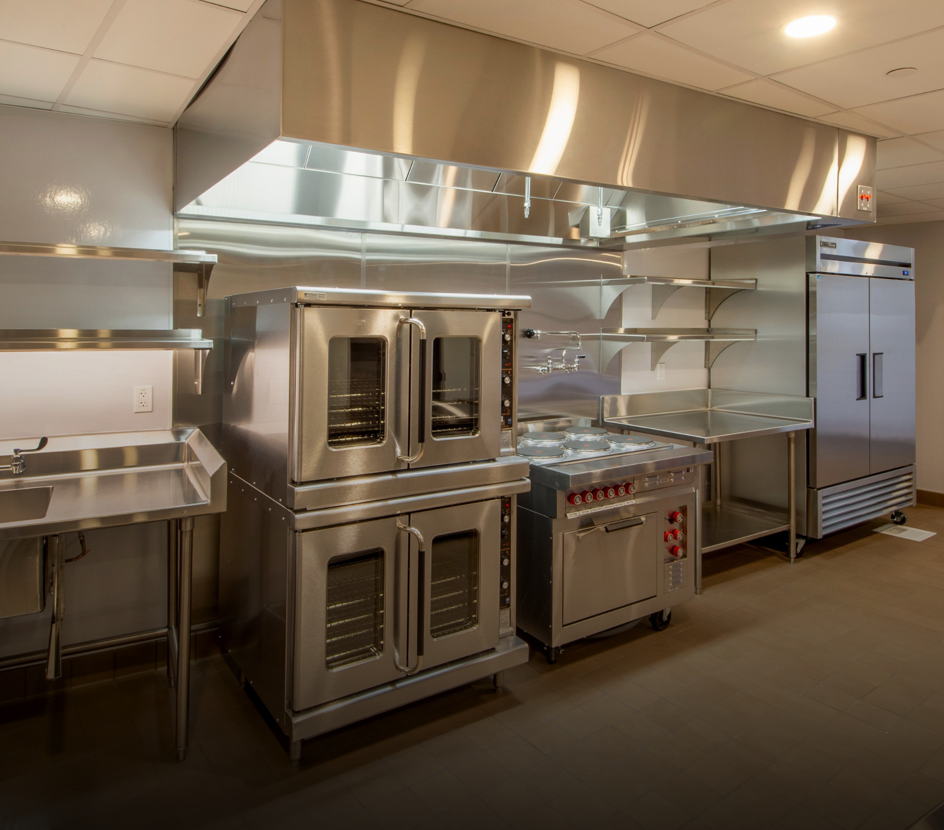 Commercial kitchen with stainless steel appliances, including ovens and a refrigerator.