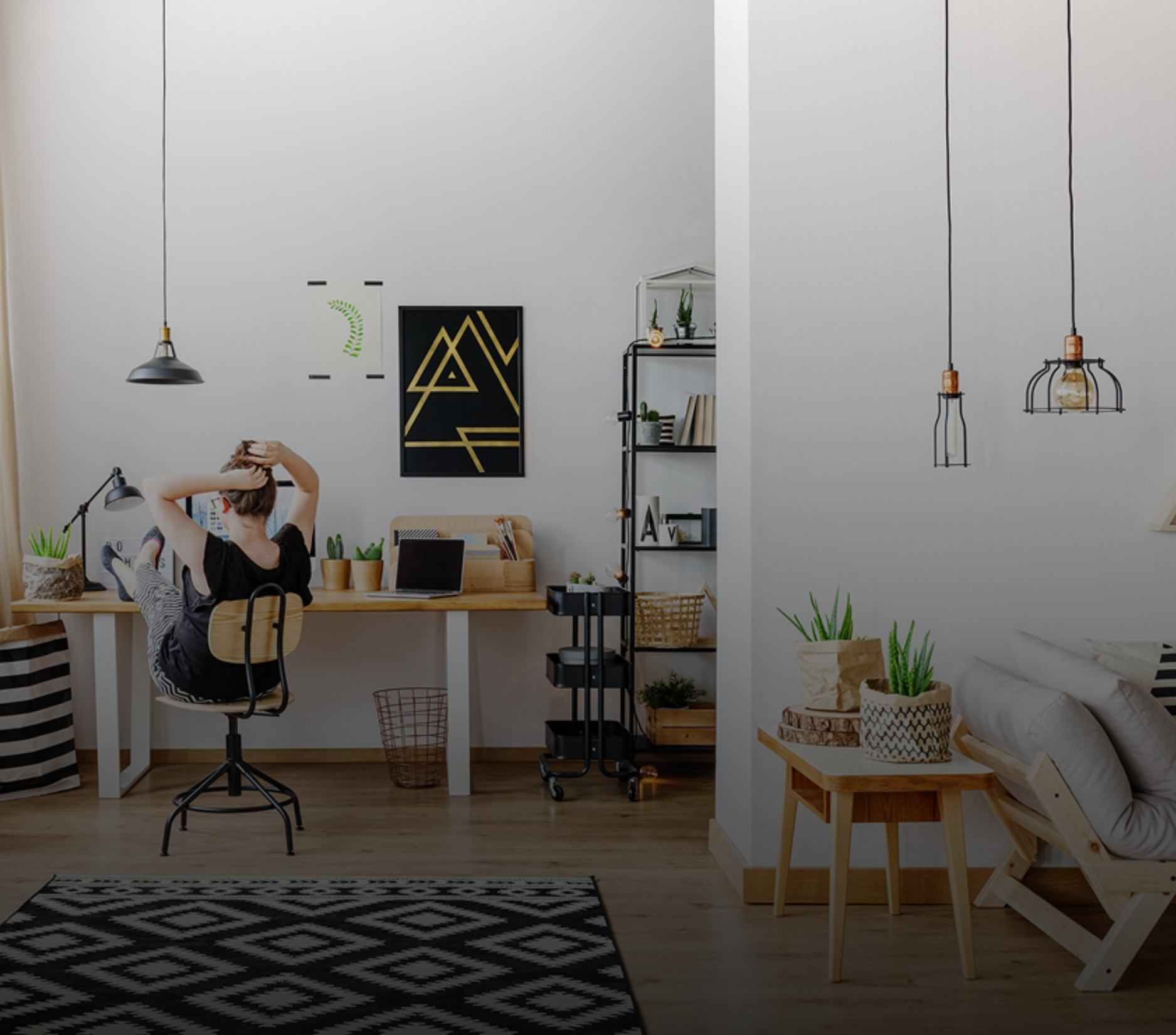 Woman relaxing at a home office desk. Black and white rug, tall white walls, two pendant lights.