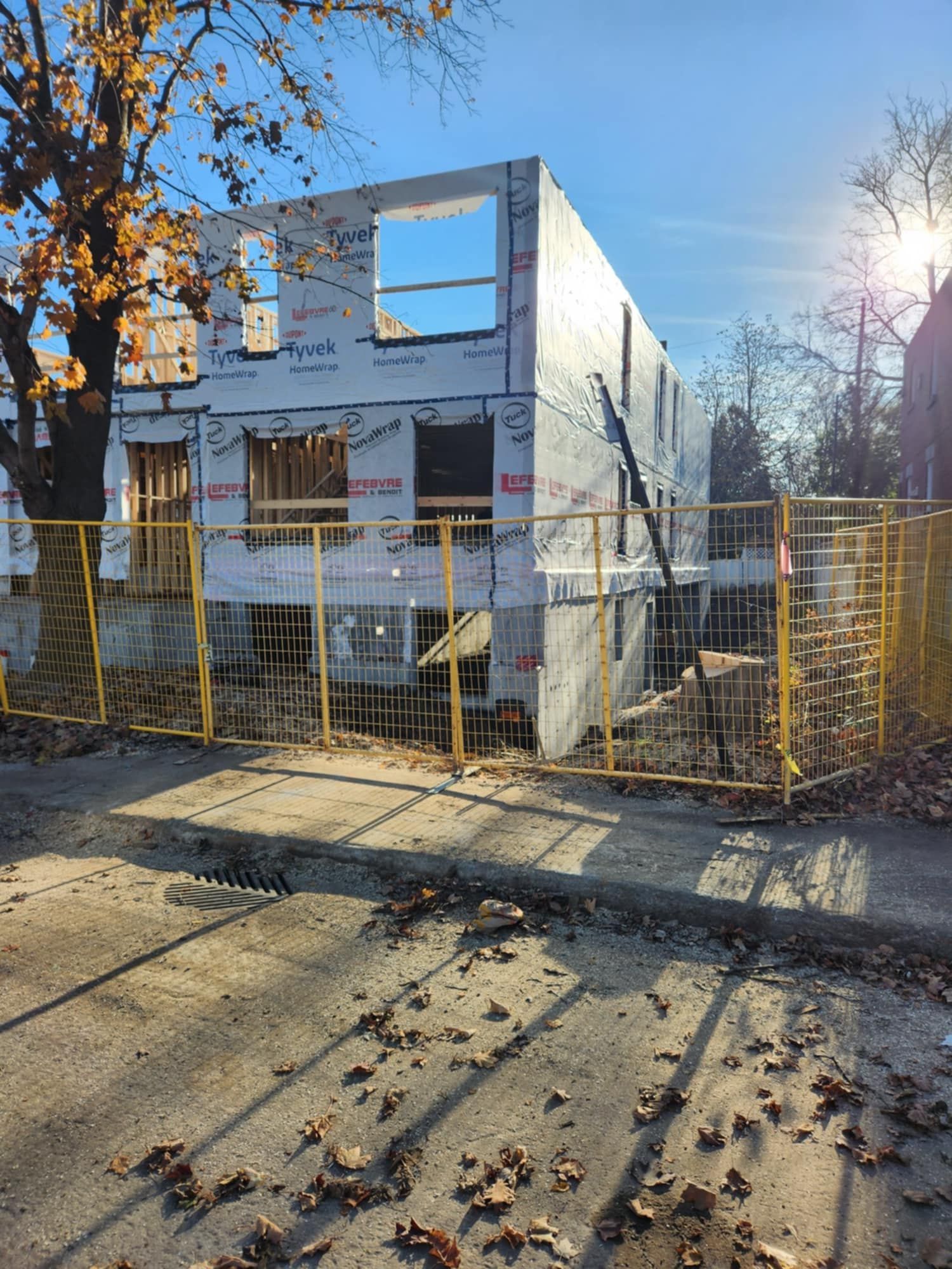 Bâtiment en construction derrière une barrière jaune. Bâche blanche et charpente apparente visibles.