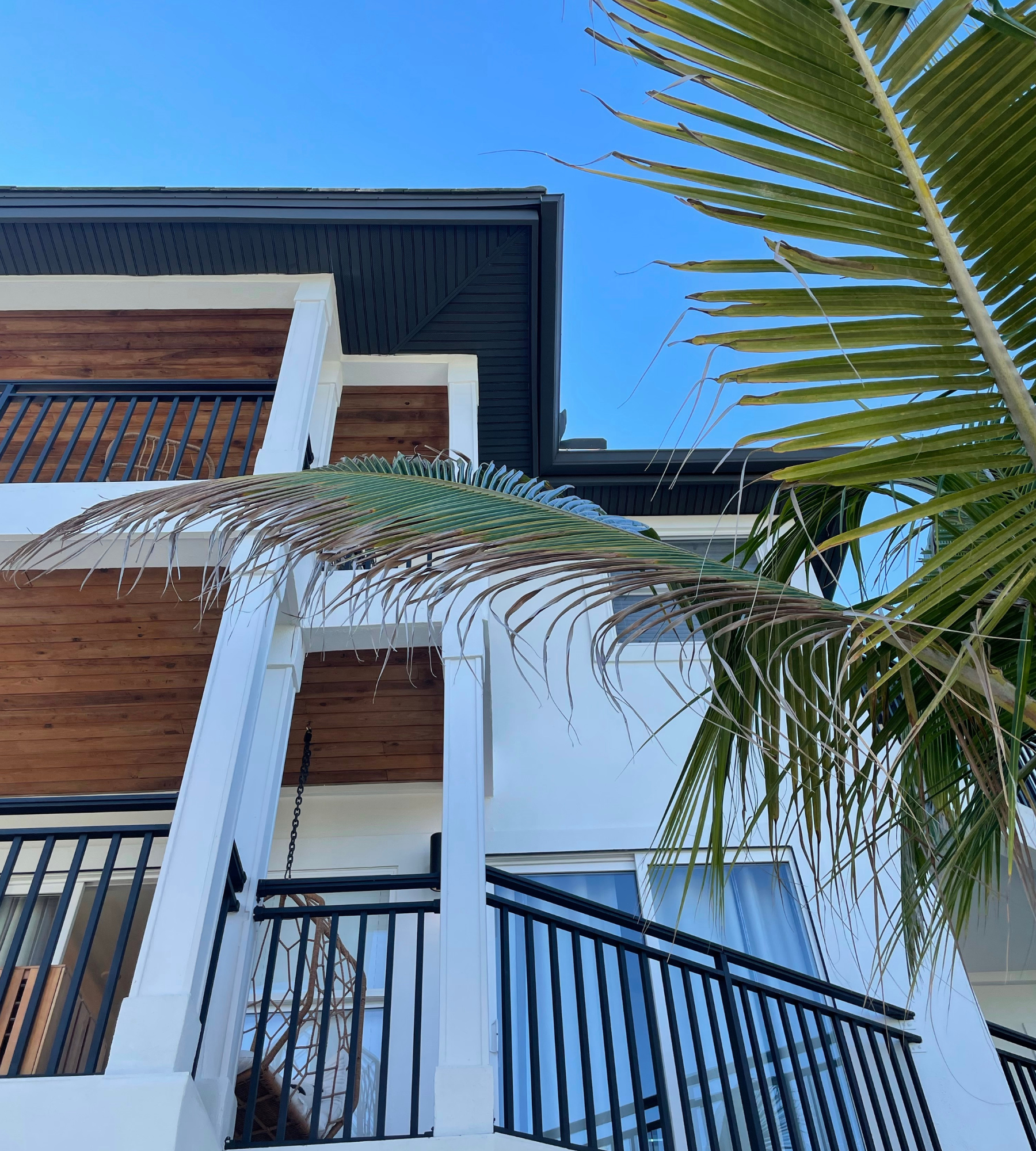A white house with a balcony and a palm tree in front of it
