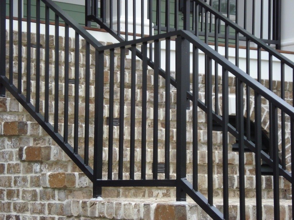 A set of stairs with a black railing and a brick wall