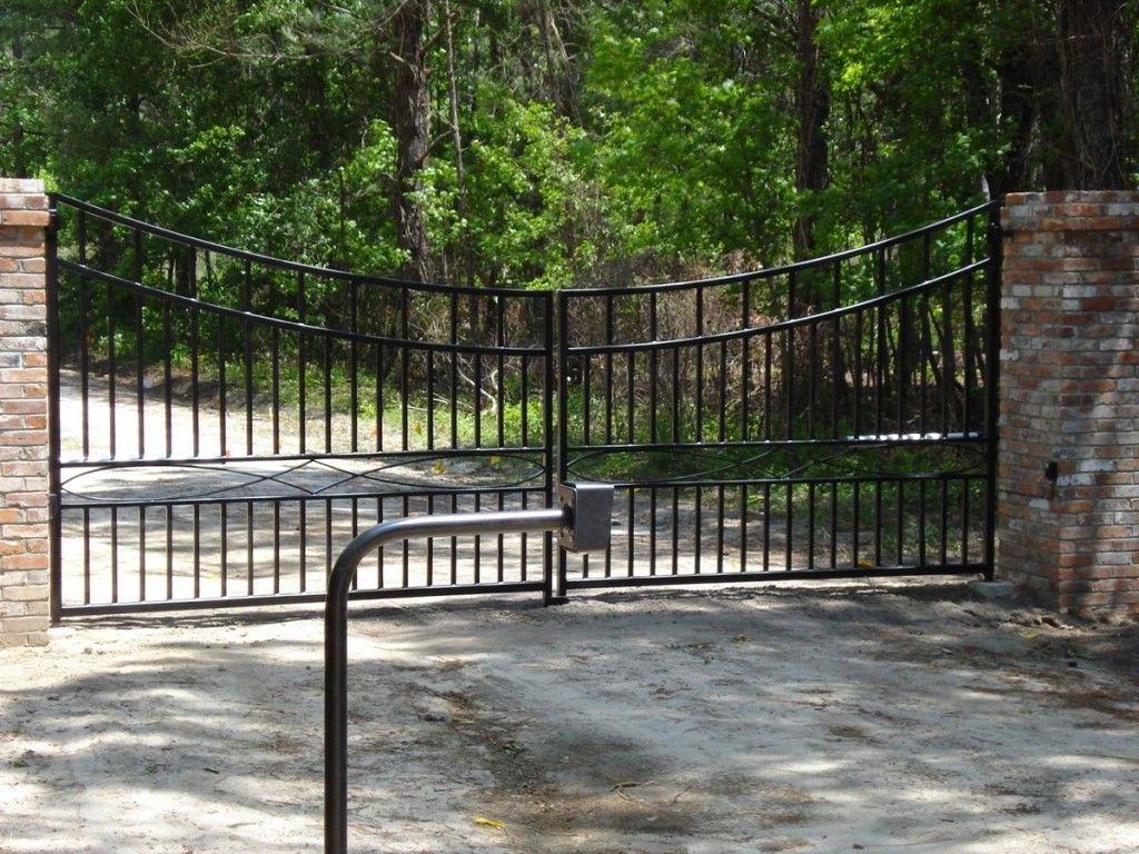 A black gate is open to a dirt road with trees in the background