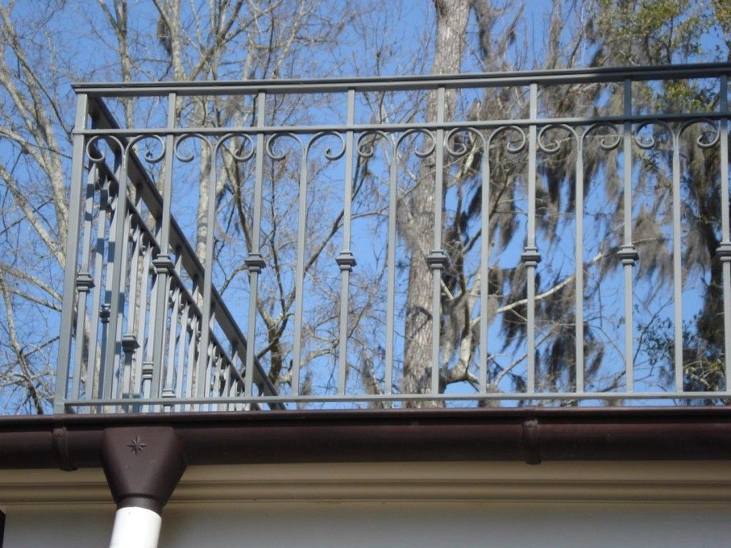 A balcony with a wrought iron railing and trees in the background