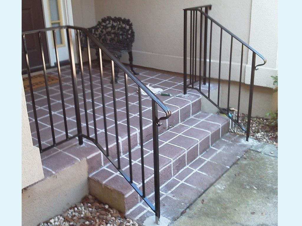 A brick porch with a wrought iron railing and stairs