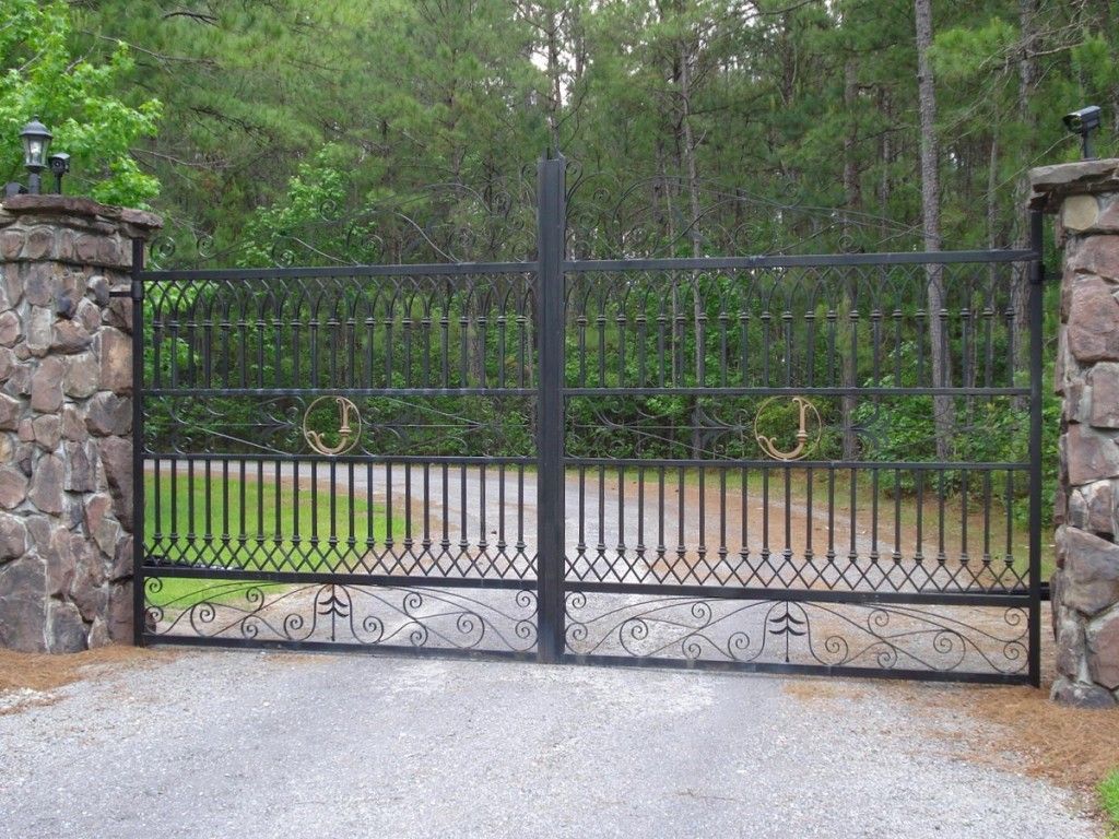 A wrought iron gate surrounds a gravel driveway with trees in the background