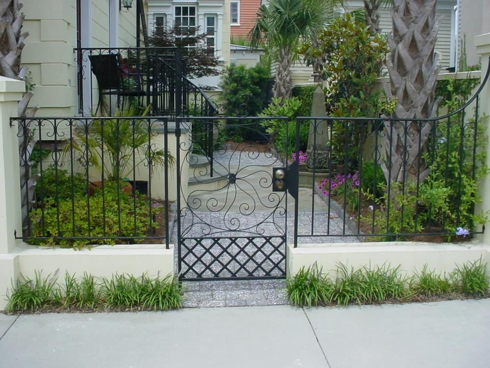 A wrought iron gate leading to a house with palm trees in the background