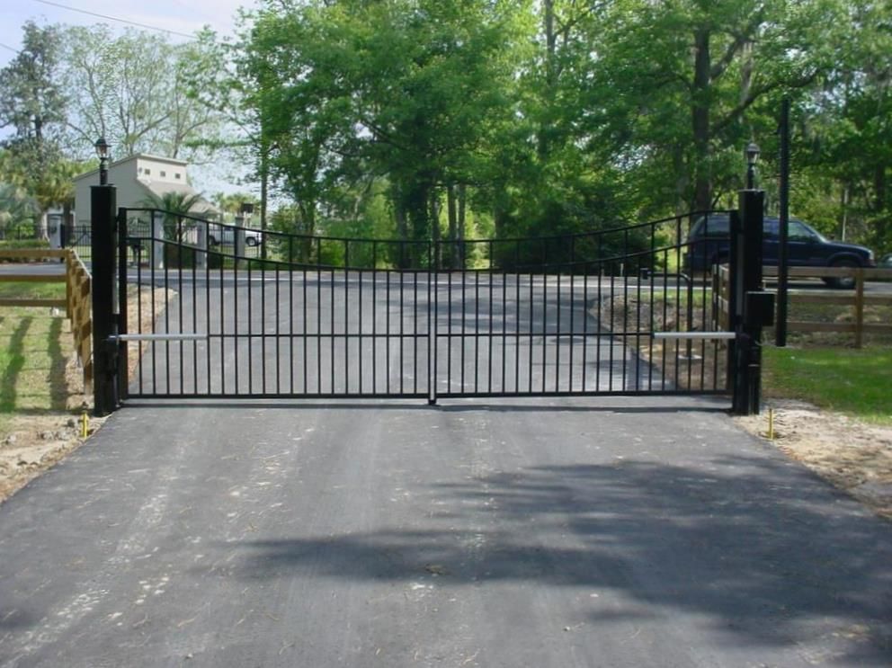 A black gate is open to a driveway with trees in the background