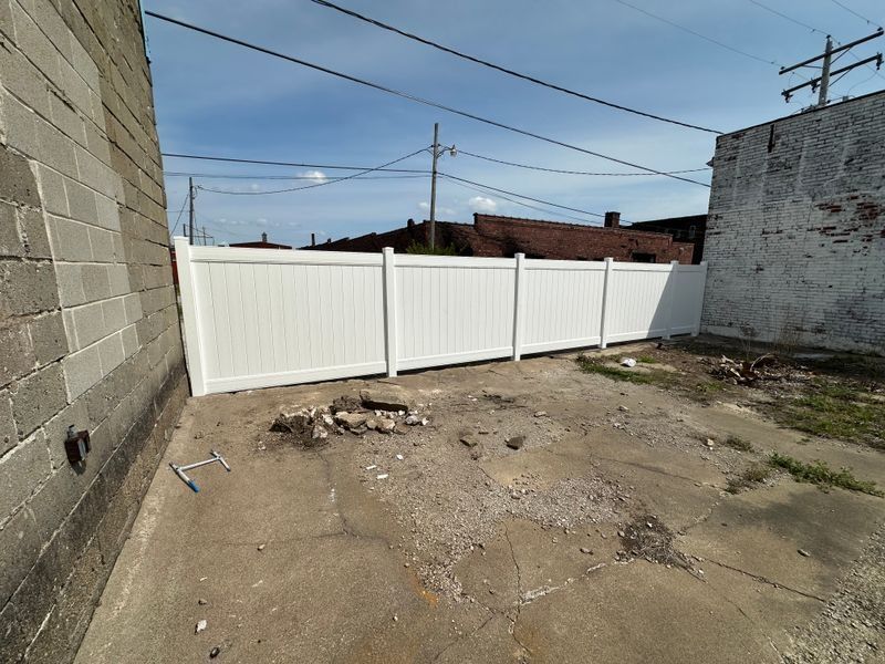 Empty dirt lot beside a white fence and cinderblock walls under a clear sky