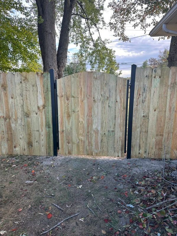 Wooden backyard fence with dark metal posts and dirt ground beneath trees