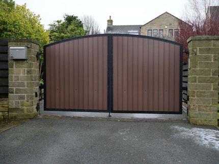 Brown double metal gate between stone pillars at a driveway entrance
