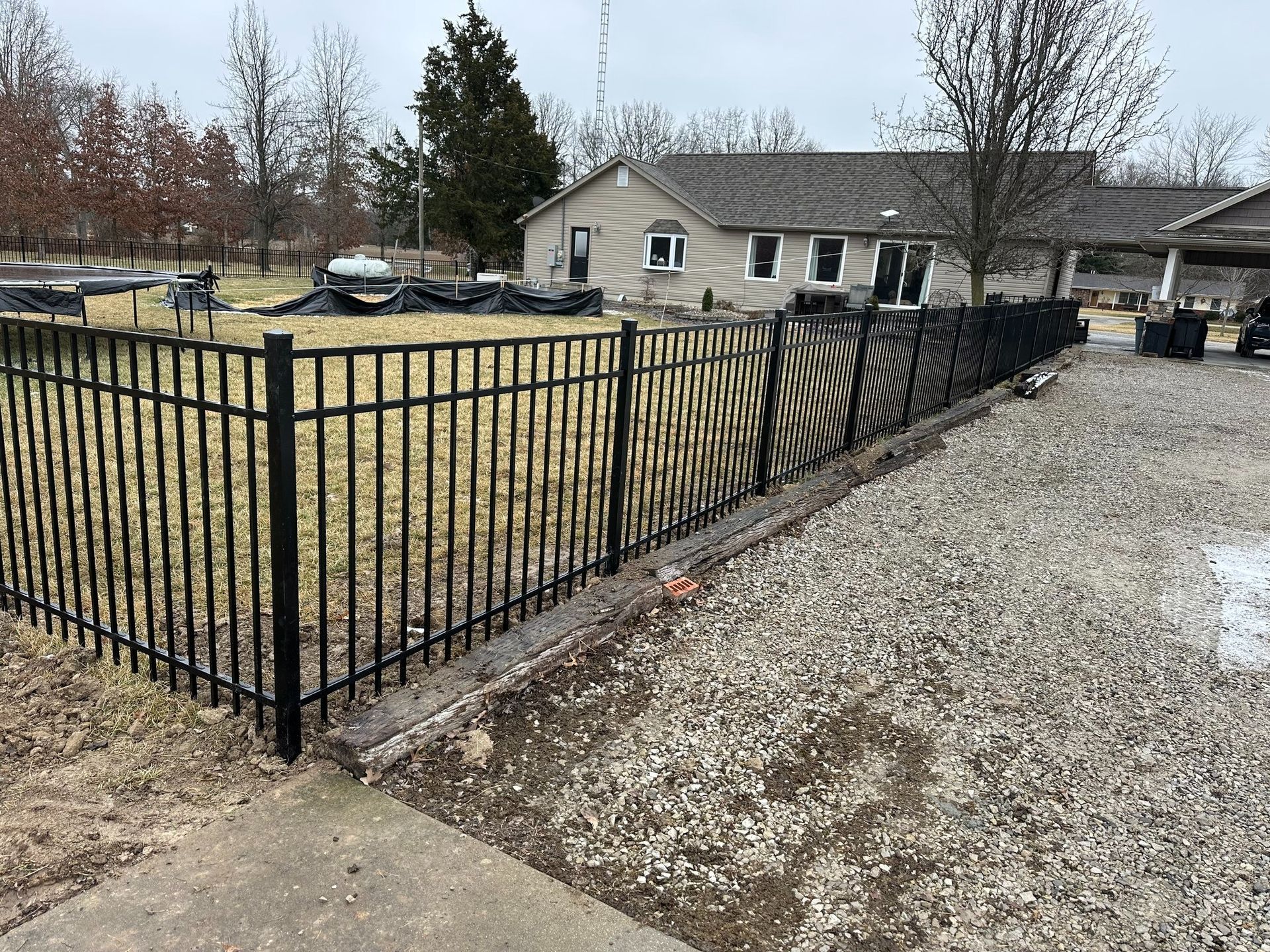 Concrete patio with black metal fence, gravel border, and leafless trees in the background