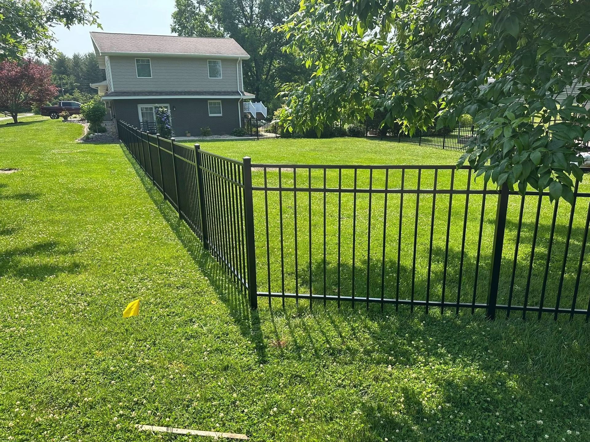Black metal fence around a green lawn with a two-story house in the background.