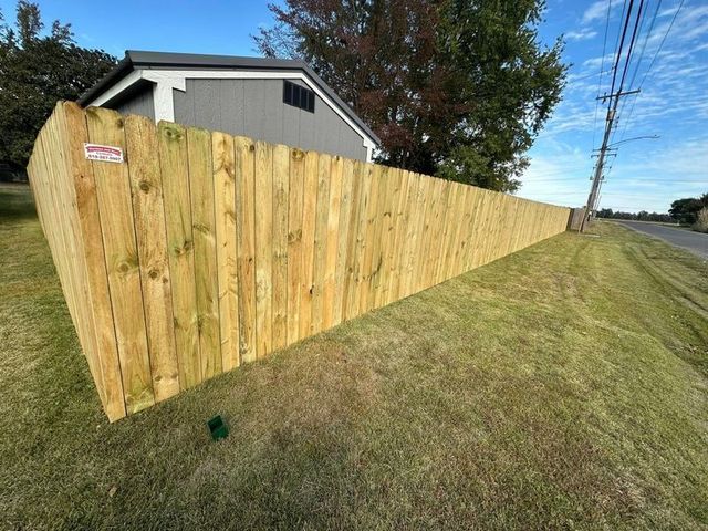 New wooden privacy fence beside a grassy yard, with a house and trees in the background