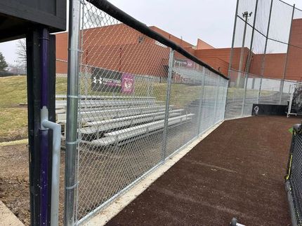 Chain-link fence beside empty bleachers and a red-brick building along a track or walkway