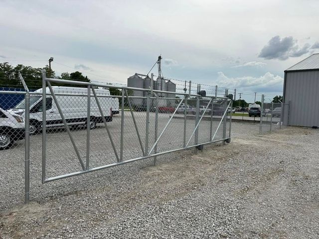 Chain-link gate beside parked vans and an industrial building on a gravel lot