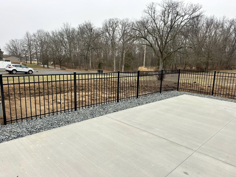 Concrete patio with black metal fence, gravel border, and leafless trees in the background