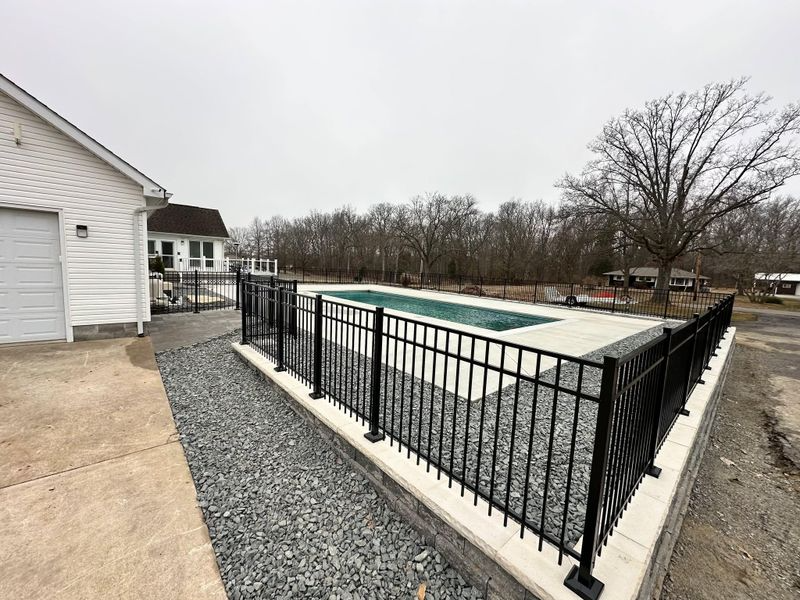 Backyard swimming pool with black metal fence beside a house on a gravel patio