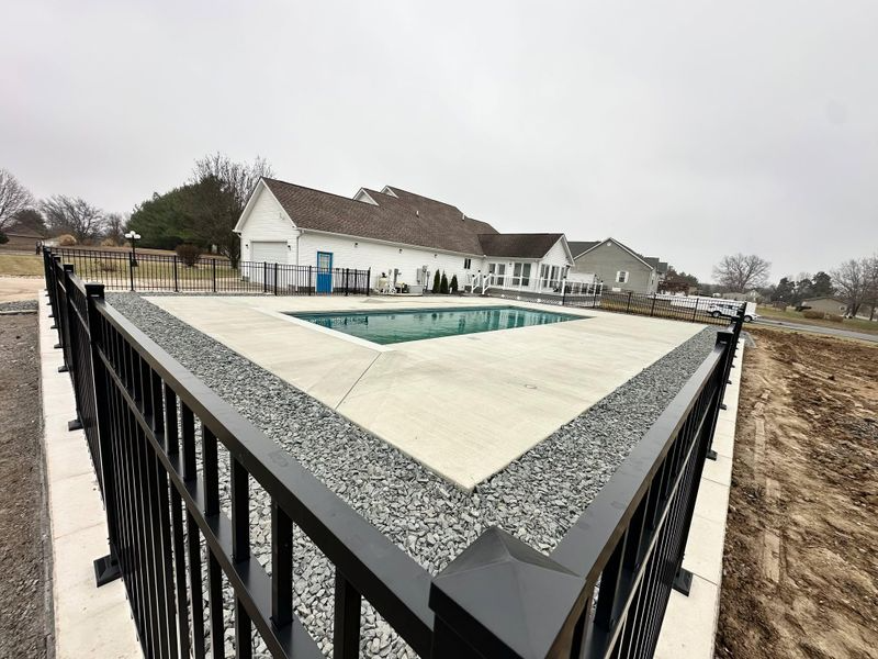 Covered backyard pool beside a white house, seen from a fenced patio under a cloudy sky