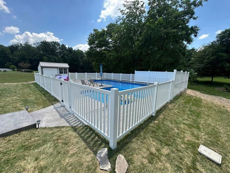 White fenced backyard pool with a small shed and grassy lawn under a blue sky
