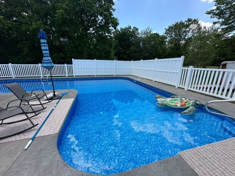Backyard pool with blue water, lounge chairs, a striped umbrella, and a white fence.