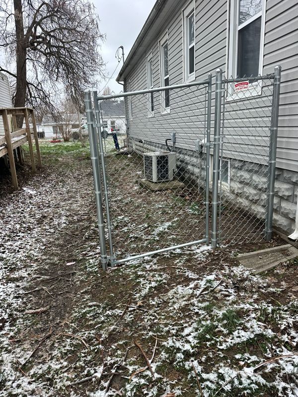 Chain-link fence gate beside a gray house in a snowy yard